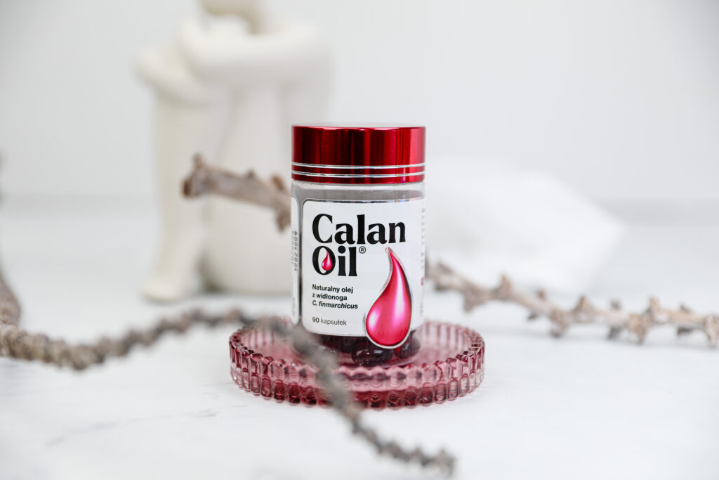 opakowanie suplementu diety CalanOil na ozdobnej szklanej podstawce